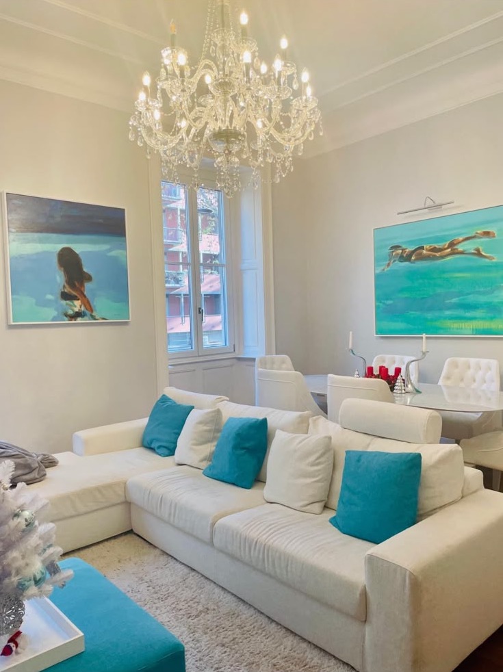 The living room: white sofa, turquoise cushions and two paintings of swimmers